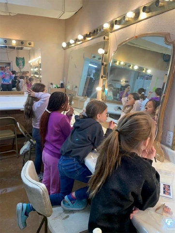 A group of children sit at a lit dressing room mirror backstage at Maples Repertory Theatre in Macon, Missouri, getting a behind-the-scenes look at the theater experience.