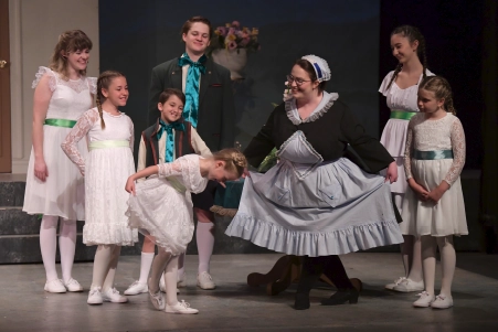 Children and teens perform on stage during a live theatre production at Maples Repertory Theatre in Macon, Missouri, with a adult actress in costume crouching to interact with a young performer as the rest of the cast looks on.