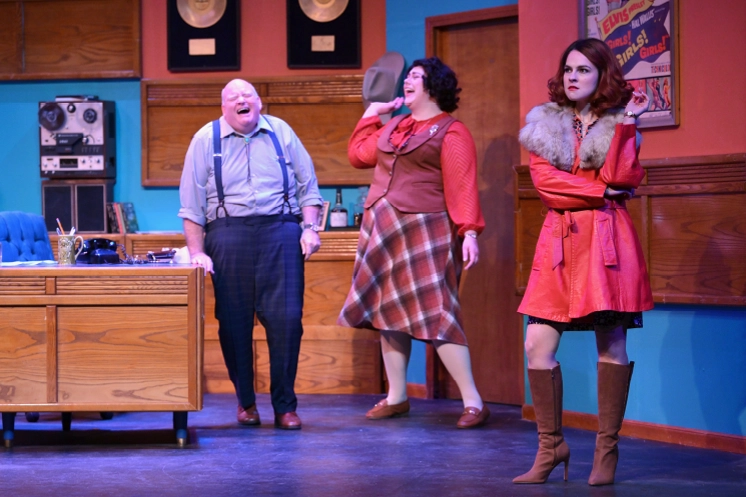 Three actors perform a comedic scene on a retro record label office set at Maples Repertory Theatre in Macon, Missouri — a man in suspenders laughs loudly, a woman in a plaid skirt reacts with surprise, and a confident young woman in a red fur-trimmed coat stands with arms crossed.
